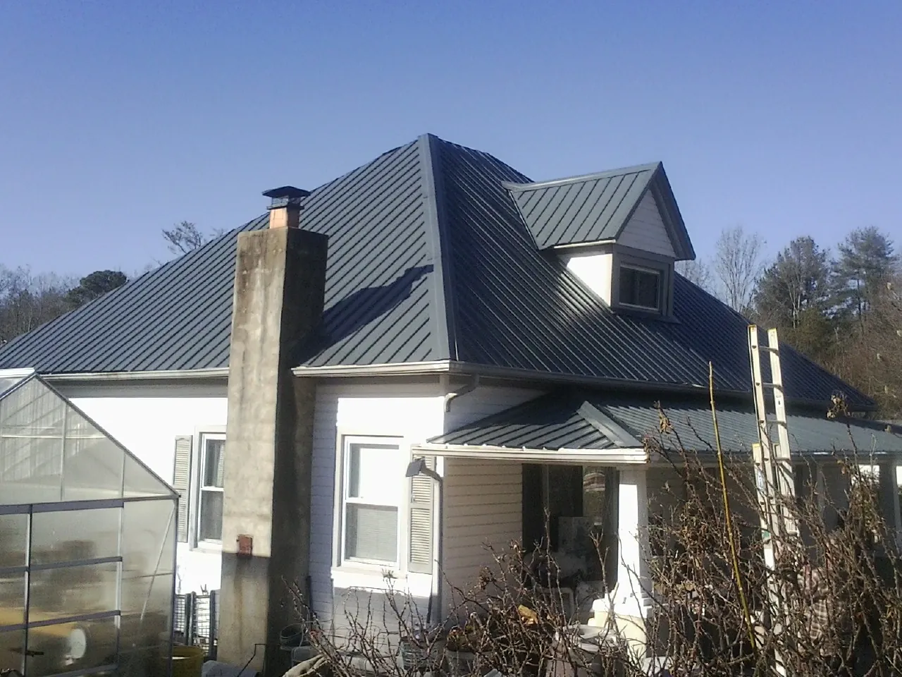 Dark blue standing seam metal roof on a white farmhouse with dormer — Slate & Tile Roof Repair by Roofing Brothers in New Era