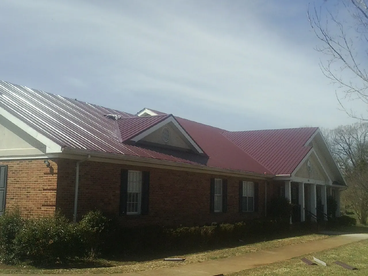 Red metal roof with gabled entries on a long brick building, from a Hail Damage Roof Repair job in New Era
