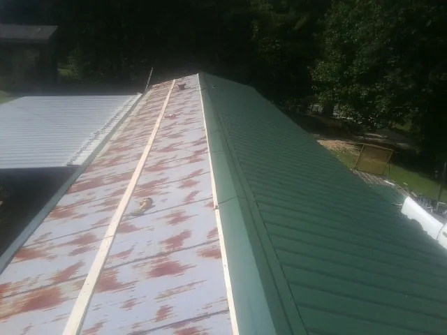 Old rusted panels beside newly installed green metal roofing — Wind Damage Roof Repair by Roofing Brothers in New Era