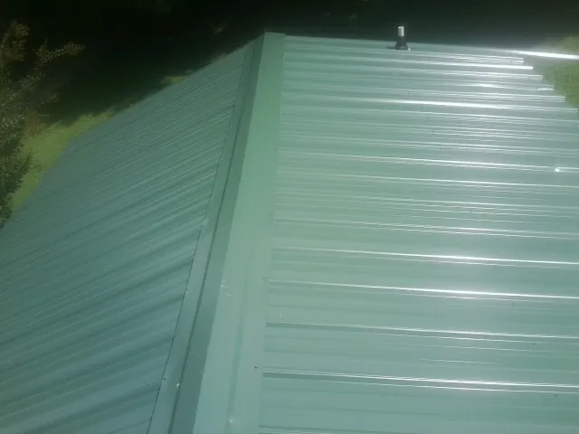 New green metal panels meeting at the ridge of a roof — Flat Roof Repair work by our crew in New Era