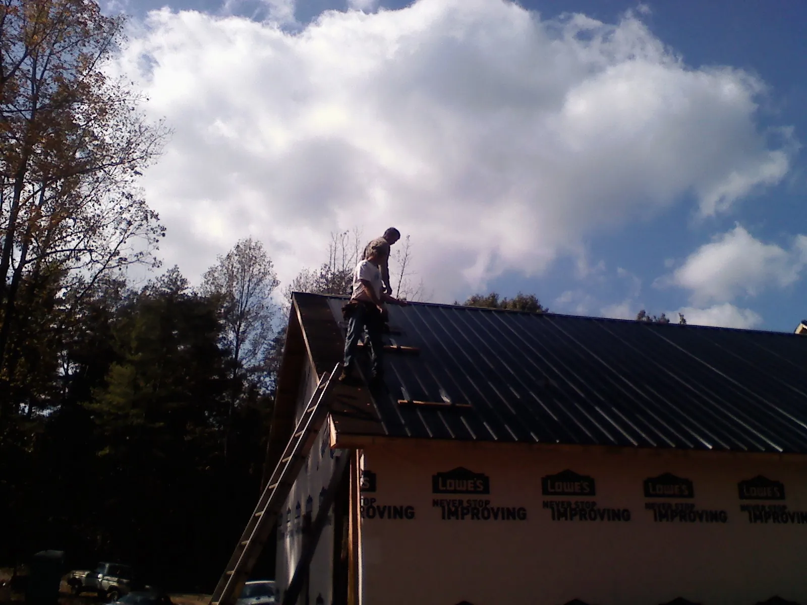 Roofer fastening dark metal panels high against a cloudy sky, from a Roof Inspection job in New Era