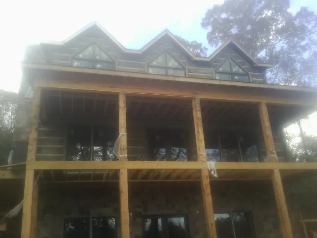 Dormers and porch framing on a large log home under construction — Roof Coating work by our crew in New Era
