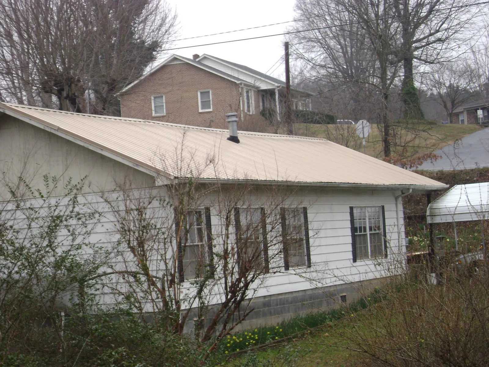 Tan metal roof on a white sided house set into a hillside — Commercial Roofing by Roofing Brothers in New Era