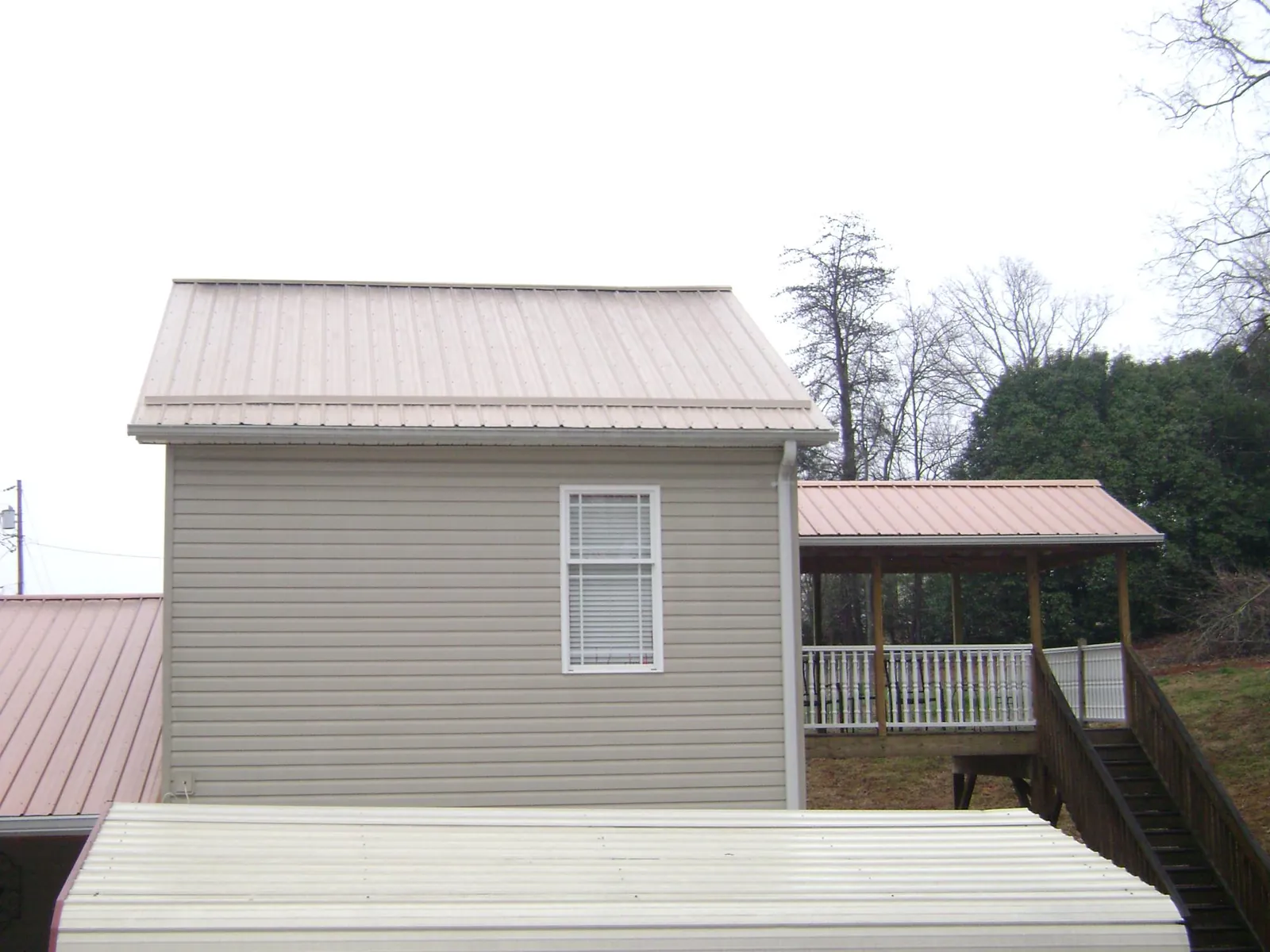 Tan metal roofs on a two story addition and attached porch, from a Roof Replacement job in New Era